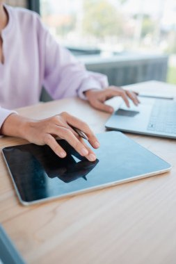 Bir insan, ahşap bir masada dijital tablet ve dizüstü bilgisayarla etkileşim kurarak, modern teknolojiyi parlak bir çalışma alanında sergiliyor..