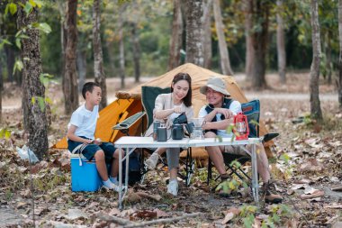 Ormanda kamp yapan aile, doğa ve ağaçlarla çevrili bir çadır ve açık hava teçhizatıyla pikniğin tadını çıkarıyor..