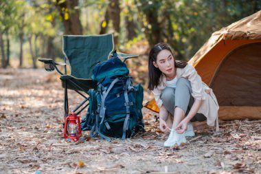 Ormandaki bir çadırın yanında ayakkabı bağı bağlayan bir kadın kamp macerasına hazır. Açık hava malzemeleri ve doğal ortam..