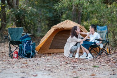 Bir anne ve çocuk kamp alanında doğayla çevrili bir çadır ve sandalyelerle bir anı paylaşırlar..