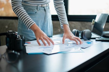 Çağdaş bir ofis ortamında çizelgeleri ve grafikleri inceleyen biri, teknolojik aletlerle çevrili..
