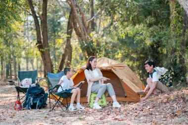 Ormanda kamp yapan bir aile. Çadırın yanında oturup doğa ve doğa aktivitelerinin tadını çıkarıyorlar..