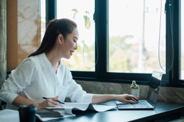 İş kadını, dizüstü bilgisayar kullanarak ve pencerenin kenarına notlar yazarak ev işlerinde çalışmaya odaklandı..