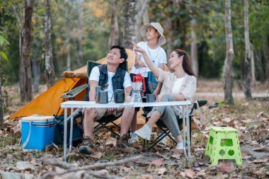 Üç kişilik bir aile, ağaçlar ve açık hava malzemeleriyle çevrili bir ormanda kamp gezisinden zevk alır..