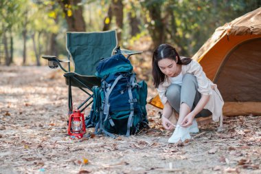 Bir kadın ayakkabılarını sakin bir orman ortamında çadırın ve kamp malzemelerinin yanına bağlıyor..