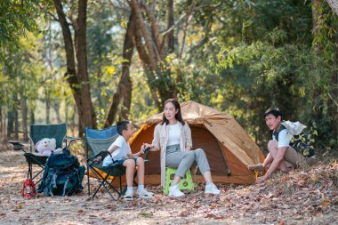 Bir kamp gezisi sırasında çevresi doğa ile çevrili, çadır ve kamp sandalyeleriyle kaynaşan bir aile..