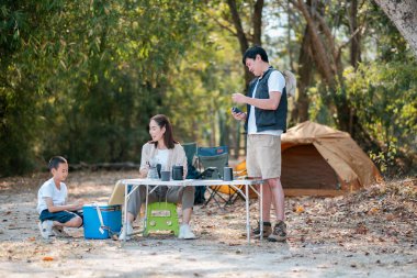 Çadırlı bir ormanda kamp yapan aile güneşli bir günde piknik ve açık hava aktivitelerinin tadını çıkarıyor..