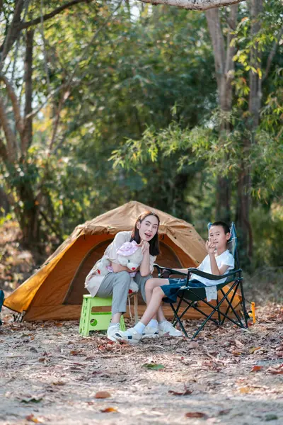 * * Bir anne ve oğul bir ormanda çadırın dışında oturuyor, doğa ile çevrili huzurlu bir kamp deneyiminin tadını çıkarıyorlar.