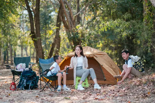 Bir kamp gezisi sırasında çevresi doğa ile çevrili, çadır ve kamp sandalyeleriyle kaynaşan bir aile..