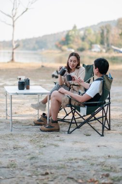 Bir çift göl kenarında dinleniyor, sakin bir açık havada kamp yaparken kahvenin tadını çıkarıyor..