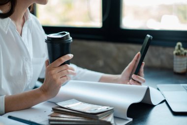 Akıllı telefon kullanan, kahve fincanı tutan, modern çalışma tarzını sergileyen bir iş adamı..