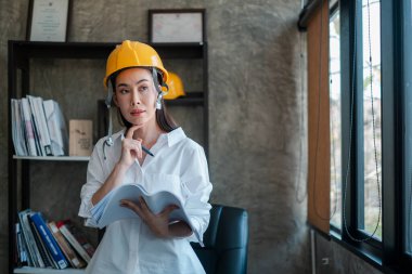 Çağdaş bir ofis ortamının planlarını analiz eden sert bir şapka takan profesyonel kadın mimar..