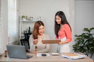 Modern bir ofiste birlikte çalışan iki kadın, belgeleri tartışıyor ve dizüstü bilgisayar kullanıyor, takım çalışması ve işbirliği sergiliyor..