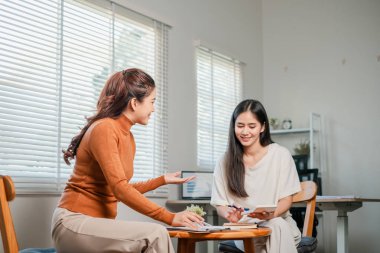 Işıl ışıl bir ofiste, masada iş tartışan iki kadın, takım çalışması ve işbirliği sergiliyorlar..