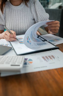 Ahşap bir masada finansal verileri ve grafikleri inceleyen profesyonel bir kadın iş büyümesi ve analizine odaklanıyor..
