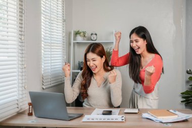 İki kadın, evde çalışırken, modern bir ofis ortamında takım çalışması ve başarı sergileyerek başarıyı neşeyle kutluyor..