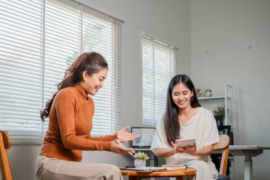 Ev ofis ortamında sohbet eden iki kadın tablet ve kahve içerken fikir alışverişinde bulunuyor..