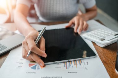 Bir tablet kullanarak ve finansal tabloları inceleyerek, modern iş analizlerini ve teknolojisini vurgulayarak ellerinizi yakın plan yapın.