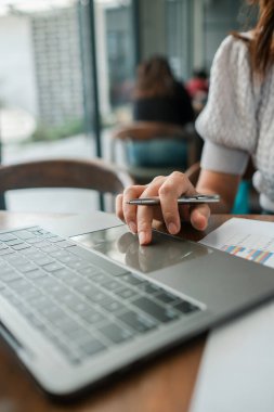Modern ofis ortamında verileri analiz etmek için dizüstü bilgisayar ve kalem kullanan birinin yakın plan fotoğrafı..