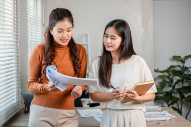 Modern bir ofiste iki kadın belge, takım çalışması ve işbirliği hakkında konuşuyor..