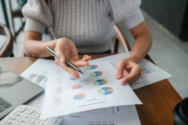 Finansal belgeleri renkli çizelgelerle inceleyen, modern bir ofiste iş analizi ve strateji sergileyen profesyonel bir kadın..