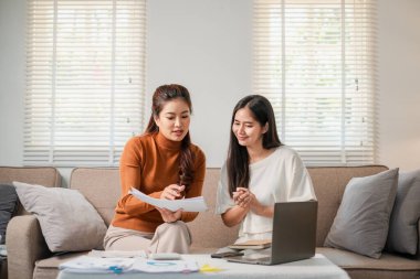 Rahat bir oturma odasında iş belgelerini tartışan iki kadın, dizüstü bilgisayarda birlikte çalışıyorlar..