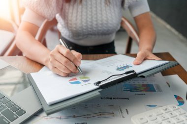 Finansal belgeleri grafik ve grafiklerle inceleyen profesyonel bir kadın, iş analizi ve stratejisini ön plana çıkarıyor.