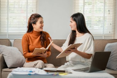 İki kadın, rahat bir oturma odasında dizüstü bilgisayarları ve defterleri olan bir proje üzerinde dostça bir tartışmaya giriştiler..