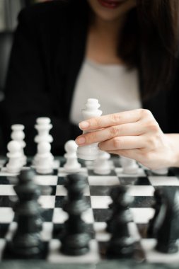 Bir kadın satranç oynuyor, klasik bir siyah beyaz tahtada beyaz bir parçayı hareket ettirmeye odaklanıyor, strateji ve konsantrasyonu vurguluyor..