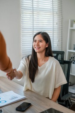 Modern bir ofisteki iş kadını, gülümseyen ve el sıkışan, belgeler ve akıllı telefonuyla..