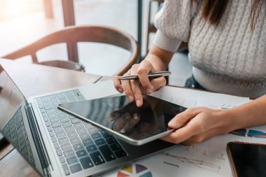 Çağdaş bir ofis ortamında iş stratejisi verilerini analiz eden, tablet ve laptop üzerinde çalışan profesyonel bir kadın..