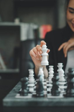 Satranç oynayan, elinde beyaz bir şahın taşını tutan, modern bir kapalı alan ortamında strateji ve konsantrasyon sergileyen birinin yakın çekimi..