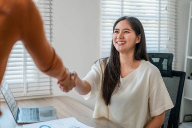 Gülümseyen iş kadını parlak bir ofiste el sıkışıyor başarılı bir ortaklığı ve işbirliğini simgeliyor..