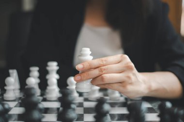 Stratejik bir oyun sırasında satranç taşını tutan bir elin yakın çekimi, odaklanmayı ve stratejiyi vurgular.