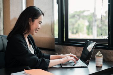 İş kadını penceresinden yeşillik manzaralı, parlak bir ofis ortamında dizüstü bilgisayarına odaklandı..
