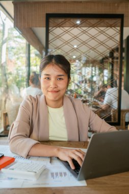 Modern dekorasyon ve doğal ışıkla çevrili bir kafede laptopuyla çalışan genç bir kadın..