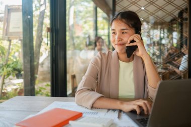 Parlak, modern ofis ortamında telefon ve dizüstü bilgisayarla birden fazla iş yapan, üretkenlik ve iletişim gösteren profesyonel bir kadın..