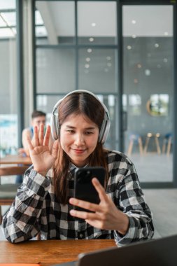 Çağdaş bir kafe ortamında telefon ve kulaklık kullanarak gülümseyen genç bir kadın..