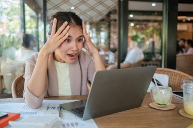 Kağıtlar ve içkilerle çevrili rahat bir kafede dizüstü bilgisayar kullanan bir kadın beklenmedik bir haber ya da başarı anı yakalıyor..