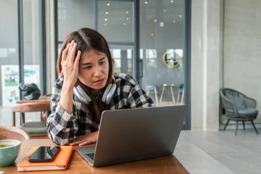 Şık bir kafede dizüstü bilgisayar kullanan, kulaklık takan, yanında akıllı telefon ve not defteri olan bir kadın..