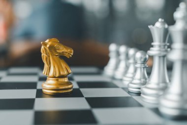 Satranç tahtasındaki altın şövalye taşının yakın çekimi, gümüş parçalarla çevrili, altını çizme stratejisi ve rekabet.