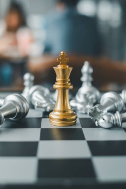 Satranç tahtasındaki gümüş parçalarla çevrili altın bir satranç kralı, strateji ve zaferi simgeliyor..