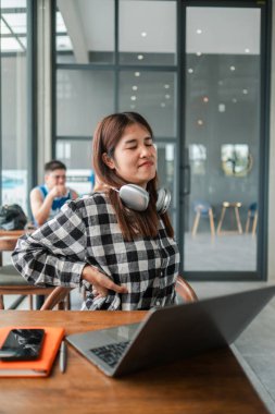 Kulaklıklı genç bir kadın modern bir kafede mola veriyor. Dizüstü bilgisayarı üzerinde çalışırken biraz dinleniyor..