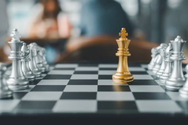 Altın kral satranç taşı satranç tahtasındaki gümüş taşlar arasında duruyor. Stratejiyi ve liderliği simgeliyor..