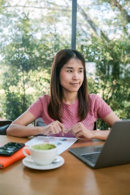 Bir kafede, elinde belgelerle çalışan genç bir kadın modern, doğal ortamında kahve molası veriyor..