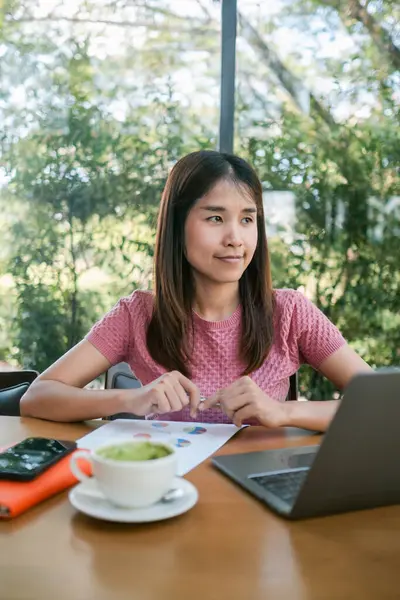 Bir kafede, elinde belgelerle çalışan genç bir kadın modern, doğal ortamında kahve molası veriyor..