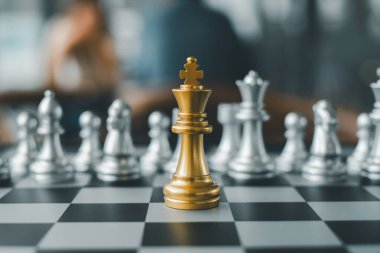 Altın bir satranç kralı gümüş parçalarla çevrili bir satranç tahtasının üzerinde duruyor. Bu da strateji ve liderliği simgeliyor..