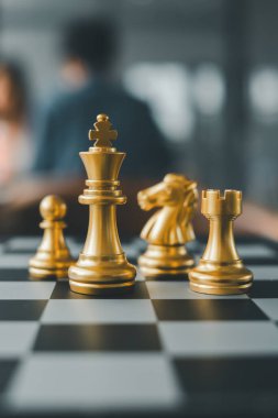 Satranç tahtasındaki altın satranç taşlarının yakın plan çekimi, arka plan bulanık bir ayarda strateji ve rekabeti vurguluyor.
