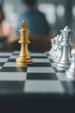 Kareli tahtada gümüş parçalarla çevrili altın kral satranç taşının yakın çekimi strateji ve rekabeti simgeliyor..