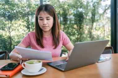 Laptop kullanan odaklanmış bir kadın ve modern bir kafe ortamında dokümanları inceleyen bir kadın..